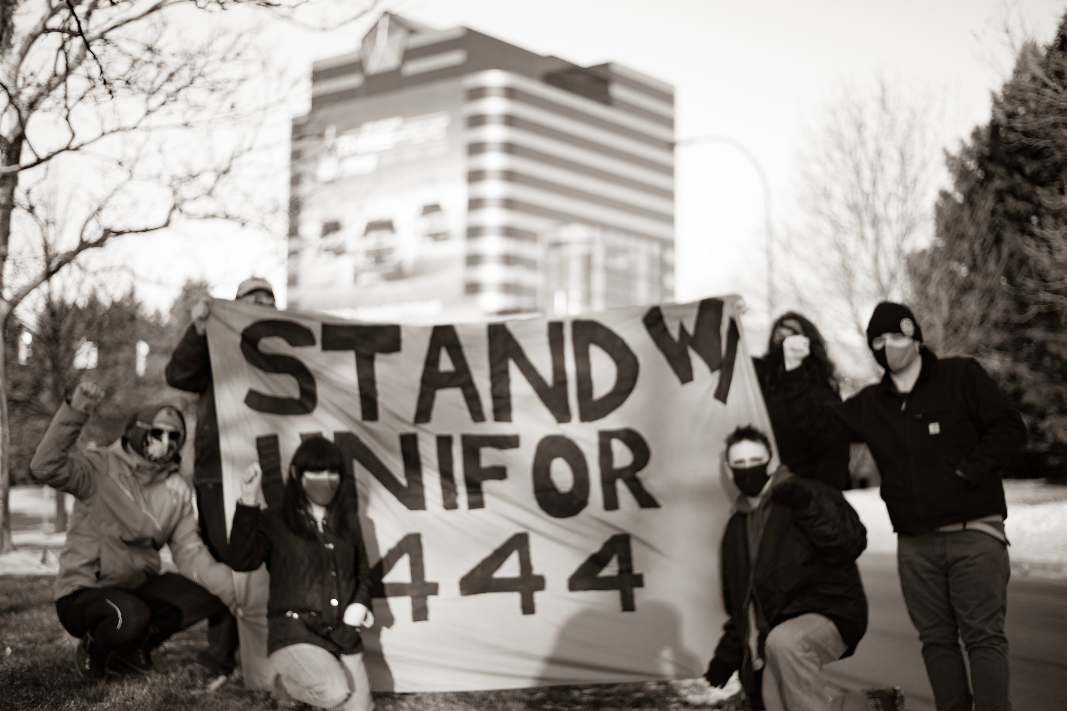 Six IWW Detroit Members stand with a banner which reads "Stand With Unifor 444."